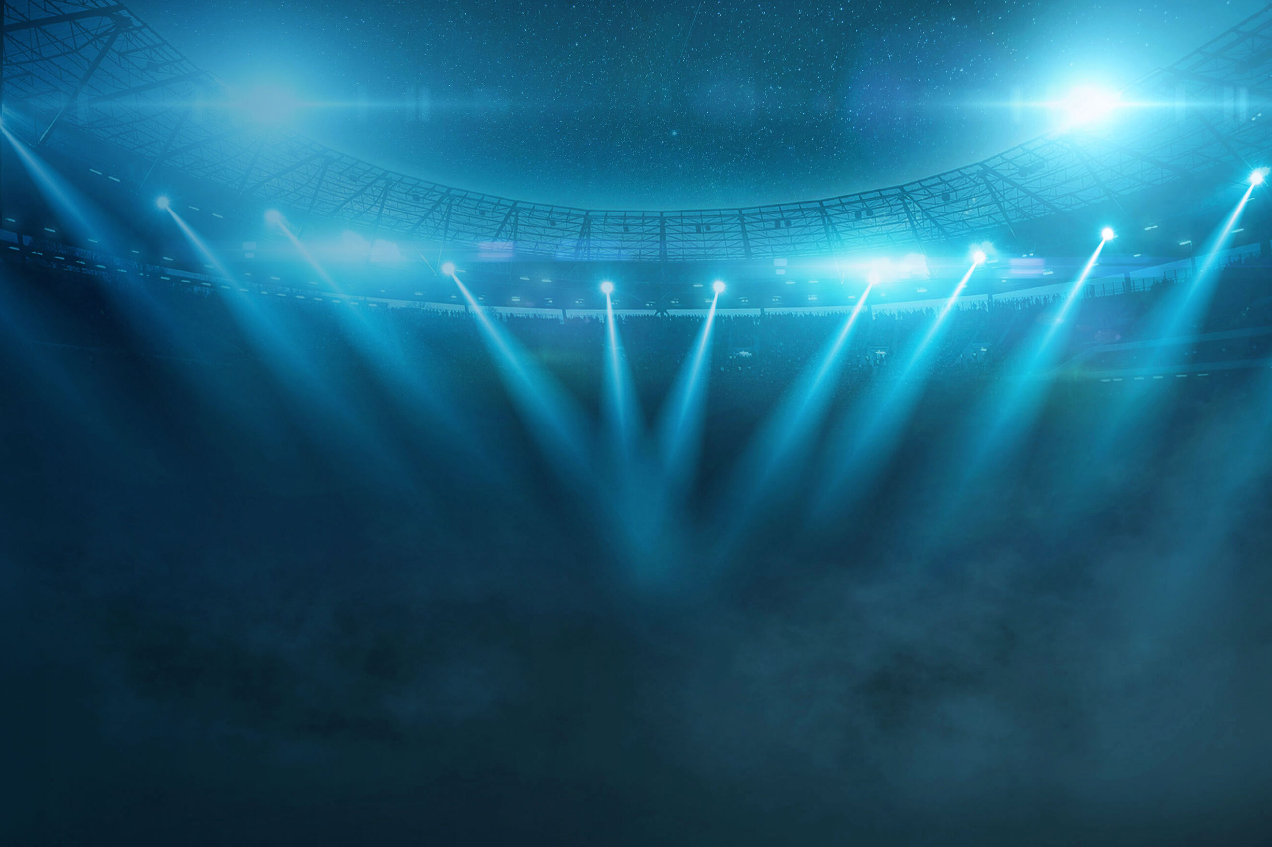 Image of a packed stadium with lights beaming onto a stage.