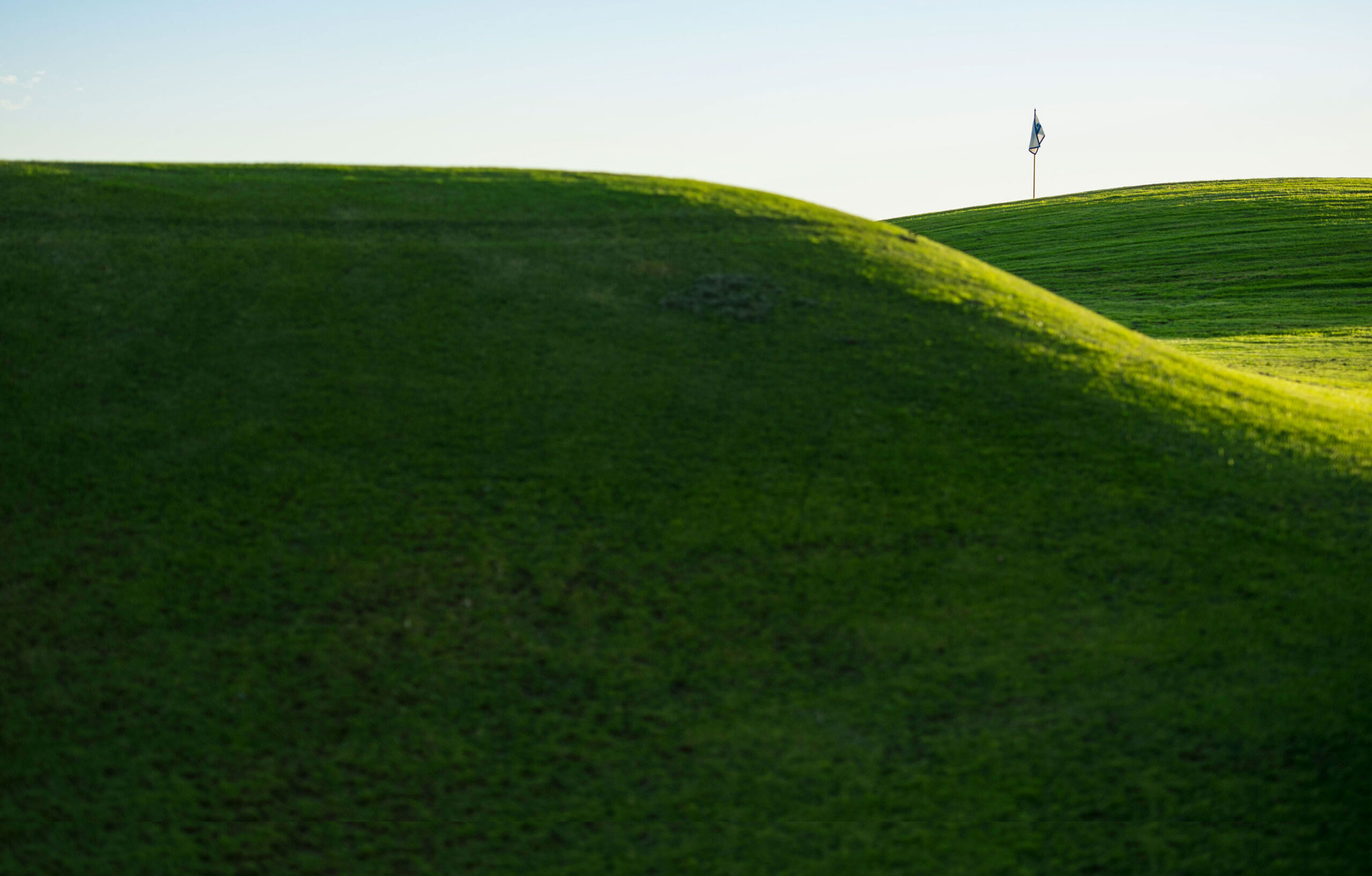 A flag atop green hills on a golf course.