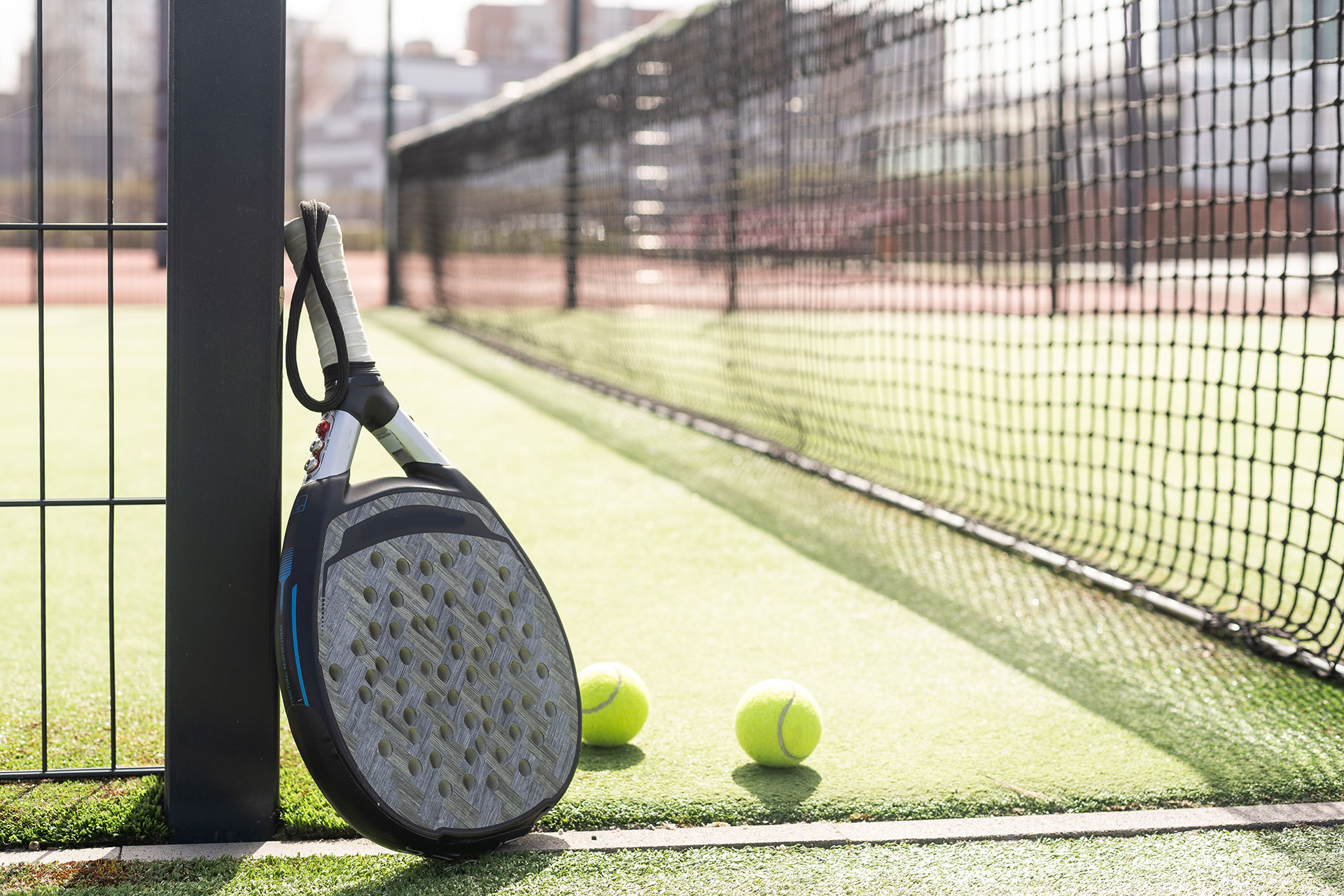 A padel racket leans against a fence at a padel court.